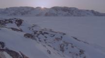 Sun Peeks Above Mountains Of Frozen Arctic Landscape