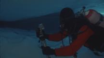 Underwater Film Maker Adjusts Light On Tripod Under Ice