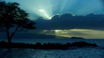 Sun Rays Behind Clouds Over Horizon, Silhouette Of Jetty With Tree