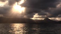 Sun Beams Through Clouds Over Water And Mountains 