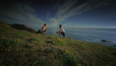 Couple practicing yoga on hillside overlooking Pacific Ocean,OR