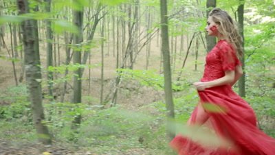Steadicam shot of a beautiful fairy tale girl in red long dress running in woods