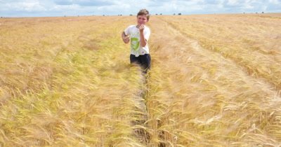 Young boy running through wheat field in sunny day