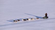 Zatzworks Cineflex Aerials Close Up Tracking Shot Dog Musher Takes A Drink While Riding On Skids Of Sled As Dog Team Races Shadow Across Frozen Surface In Western Alaska Bering Sea Area Zoom To Extreme Wide Shot