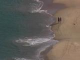 Two People Walk Along A Beach, Shot From Above