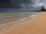 Tropical Ocean Waves Lap On Orange Sand Beach With Dark Storm Clouds Approaching.