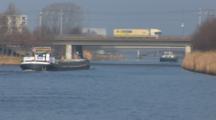 A Cargo Ships Continues Down River And Under A Bridge