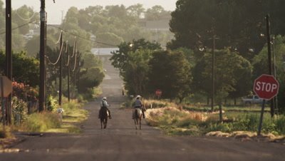 Static shot of cowboys riding horses along a street in the USA