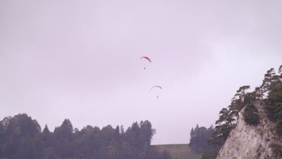 Long distance shot of two paragliders hovering over trees in Switzerland