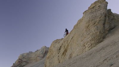 Slow motion of guy riding mountain bike off rocky cliff down a steep rocky slope.