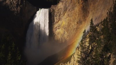 Scenic of the lower falls of the Yellowstone.  Sunrise shot of the waterfall with a vibrant rainbow in the canyon and the colors really showing in the canyon walls.  Med-Wide.