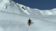 A Snowmobiler With A Snowboard Rides Uphill.