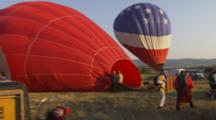 Hot Air Balloons Fill While Guys In Flight Suits Stand And Wait.