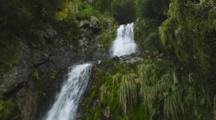 Waterfalls Off Vegetated Steep Cliff. Wide Rushing Stream Through The Rainforest. Pan From Top To Base. South Island, New Zealand.
