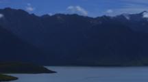 Shot Pans Left To Right. Lake Hawea With Silhouetted Mountains, Blue Sky And Clouds.