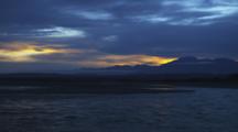 Coastal Lagoon Flows Out To Sea At Sunrise. Clouds Top The Distant Mountains, Okarito, New Zealand.