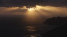 Sun Rays Stream Through Dark Clouds At Sunset Over Coast