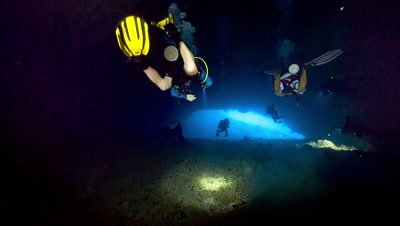 Divers swim through underwater cavern