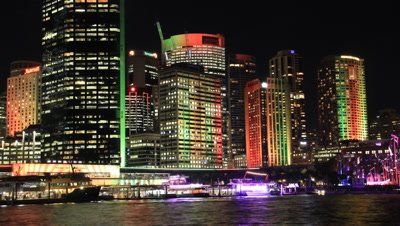 Sydney Australia city scape skyline timelapse shot at night during the vivid festival. The buildings during the Vivid festival have colourful lights that are reflecting of the harbour water.