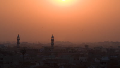 Wide angle establishing shot over Jaipur's traditional rooftops busy with birds as hazy orange sun dips and sets over dusty skyline,India
