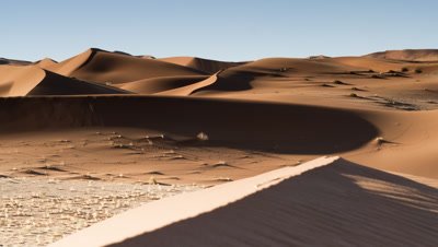 Medium wide angle desert dune landscape with sand blowing in foreground as shadows move over throughout the day and night falls