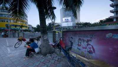 Mid shot busy street corner with palm tree and lady sat on sidewalk beneath it featuring Chinese poster Xinghong China