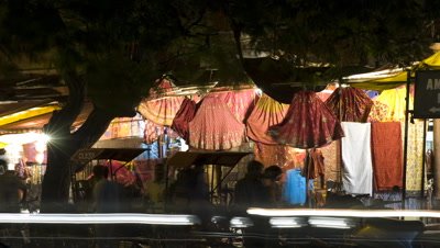 Medium wide angle street stalls selling colourful skirts with traffic passing constantly and tuk tuks coming and going at Hawa Mahal Roundabout