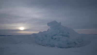Close up sea ice with cloudy arctic sun dipping behind ice at Grise Fjord