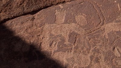 Close up on rock face as diagonal shadow moves across rock revealing ancient rock engravings
