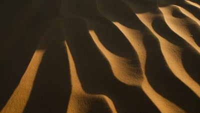 Close up pan over sand dune from black as shadow lifts to reveal golden orange stripey sand ripple patterns