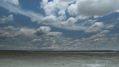 Wide angle fluffy white rain clouds, cumulonimbus, in blue sky travelling fast over vast Etosha salt pan