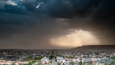 Wide angle dramatic monsoon clouds dropping showers of rain over Jaipur city then sun and beautiful god rays appear