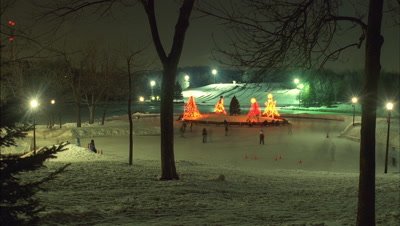 Medium wide angle looking down to people skating on frozen lake in park with illuminated simple modern Xmas trees -matches RK10221 and 10223