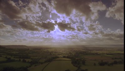 Wide angle rain clouds and sun rays move rapidly towards camera over British countryside, fields and hills with glimpses of River Severn from Coaley Peak viewpoint