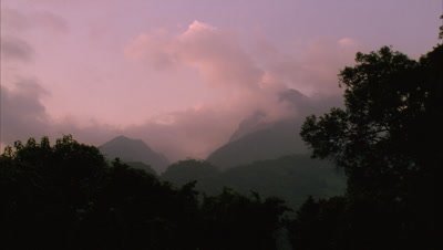 Medium wide angle looking up to peaks of Ruwenzoris as pink sun fades and cloud dissipates