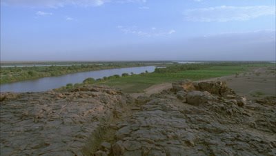 Wide angle black night sky lifts to morning light revealling view from rocky outcrop along River Nile showing desert meeting green cultivation belt