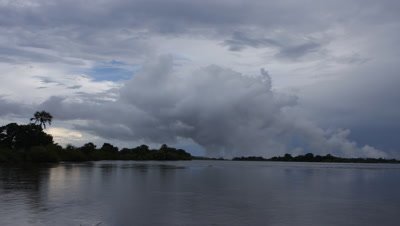 Wide angle looking across calm river early evening to the rising spray of Falls on horizon with spray funnelling dramatically up to join other clouds