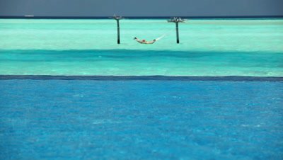 Couple in ocean hammock beyond swimming pool, Maldives, Indian Ocean